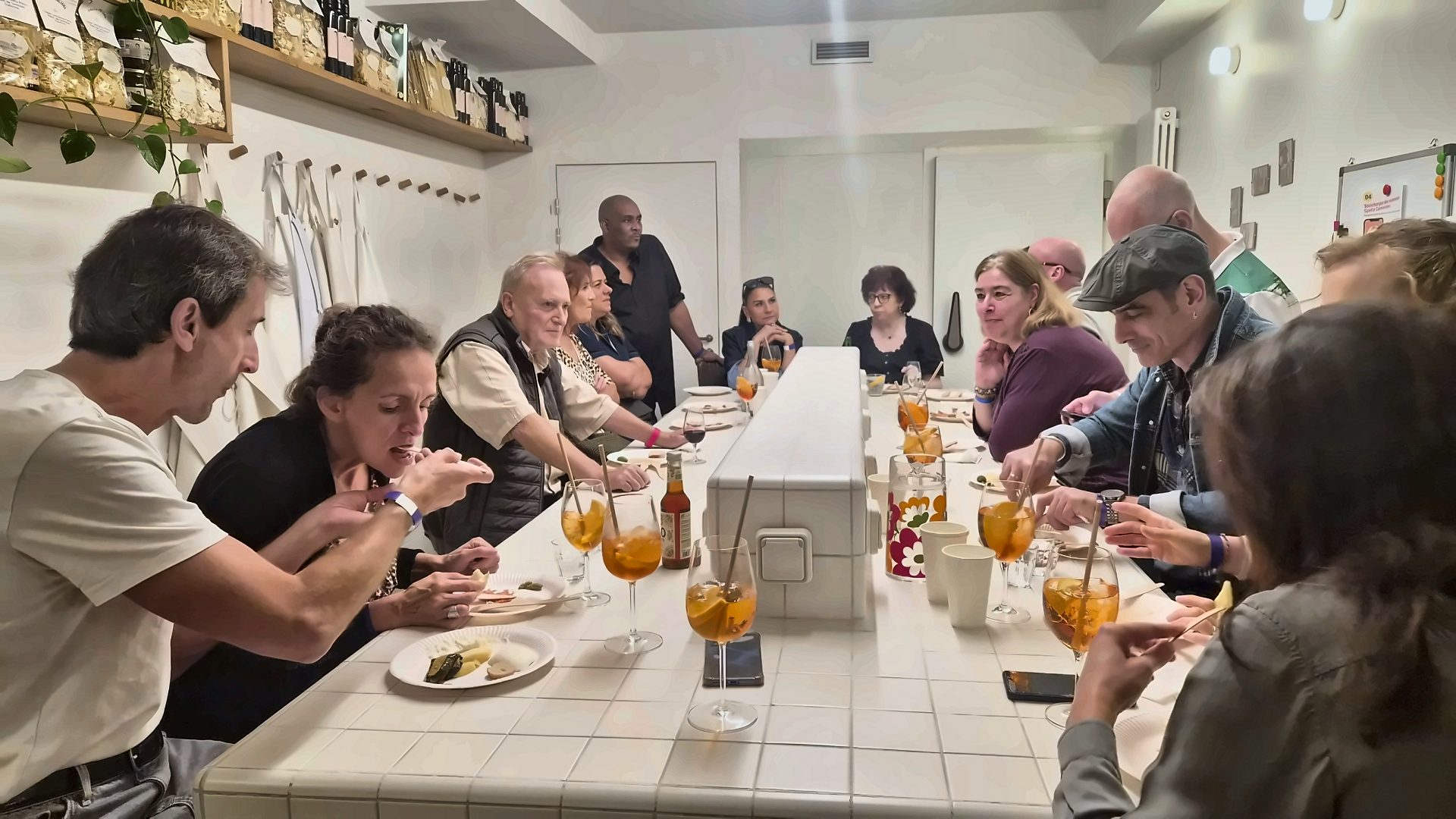 Convives autour d'une longue table carrelée lors d'un Aperitivo Italiano Spritz Connection à Paris, verres de spritz et assiettes de dégustation